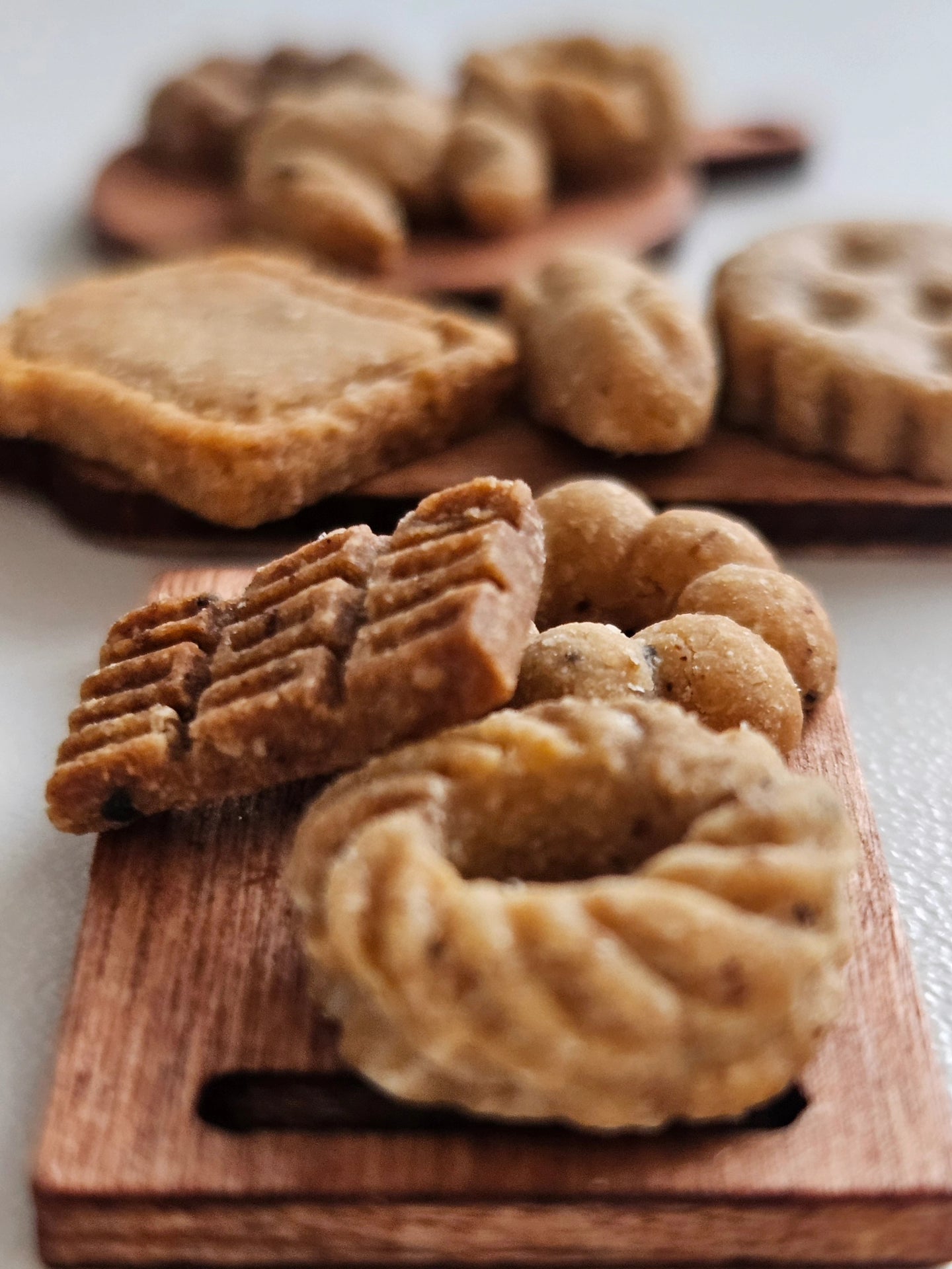 Assorted dog cookies on a wooden board with a blurred background. Minis for minis by fluffy fluff